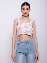 Top blanco con estampado floral en tonos naranja y lila, de corte cropped y breteles anchos.