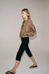 Camisa fluida de Zara Woman Collection, confeccionada en hilatura con mezcla de viscosa en tono tostado. Presenta cuello redondo, mangas largas con puños elásticos y diseño fruncido en la parte delantera. Dispone de cierre frontal con botones ocultos por solapa.