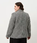 Blazer de sastrería confeccionado en tejido tweed con estampado pied de poule en blanco y negro. Presenta cuello con solapa, cierre frontal con un botón, mangas largas y bolsillos frontales con solapa.