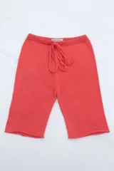 Biker de tejido de punto en color coral, con cintura elástica y cordón ajustable. Presenta un diseño de corte recto y acabado artesanal.