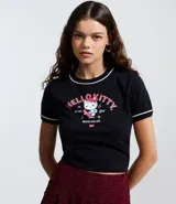 Remera negra de algodón con cuello redondo y bordes en contraste color blanco. Presenta estampa frontal de Hello Kitty en estilo skater con detalles en rosa y blanco.