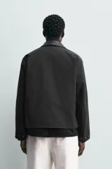 Sobrecamisa de corte relajado color beige, con cuello solapa en efecto piel de color negro. Presenta cierre frontal con cremallera, bolsillos de vivo en la cadera y mangas largas con puños ajustables.