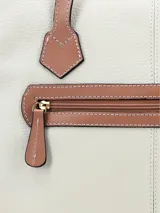Cartera tipo tote de cuero color off-white con asas largas y detalles en tono tostado. Cuenta con un pequeño logo metálico dorado en la parte inferior frontal.