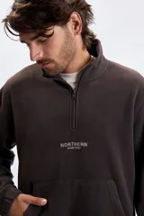 Buzo de polar color marrón con cuello alto y cierre frontal parcial. Presenta un bolsillo frontal tipo canguro y un estampado pequeño en el pecho con el texto 'NORTHERN ADVENTURES'. Cuenta con puños elásticos.