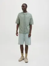 Polo de punto verde con rayas verticales blancas, corte relajado, cuello tipo camisa, cierre con botones y mangas cortas.
