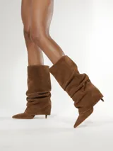 Bota de caña media confeccionada en gamuza color camel, con diseño fruncido, punta fina y taco aguja pequeño.