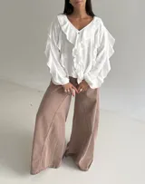 Blusa blanca de corte holgado con escote en V, decorada con volados frontales y en las mangas. Presenta mangas largas con puños elásticos y cierre frontal con botones.