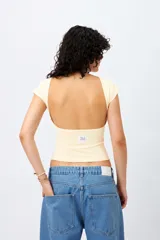 Top de manga corta color amarillo claro, con escote redondo cerrado, ajuste al cuerpo y diseño de espalda abierta.