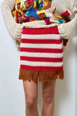 Minifalda tejida a mano en hilo de algodón, con diseño a rayas horizontales rojas y blancas, y flecos marrones en el ruedo.