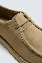 Zapato de cordones para hombre confeccionado en piel con acabado de serraje en color beige. Presenta un detalle de bordón en el empeine, horma redonda y una suela track a tono.