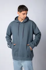 Buzo canguro oversize de tela friza, color negro, con capucha, cordones ajustables con logo y bolsillo frontal tipo canguro.