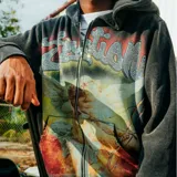 Campera con cierre frontal, confeccionada en algodón con efecto acid wash en color negro. Presenta un diseño gráfico central de un ángel con arco y flecha, acompañado por la palabra 'Emotion' escrita con apliques de strass.