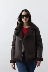 Campera tipo gamulán de símil cuero color marrón oscuro, con interior y solapas de corderito al tono. Presenta cierre frontal cruzado, bolsillos con cierre metálico y hebilla ajustable en el cuello.
