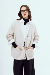 Cardigan de punto color beige, con escote en V, cierre frontal de botones carey, mangas largas y bolsillos frontales aplicados.