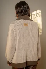 Campera de punto tipo cárdigan con cierre frontal de doble cursor, confeccionada en lana. Presenta un diseño bicolor con cuerpo en tono gris claro y detalles en azul marino en el cuello, la franja central, los bolsillos y los puños. Posee mangas largas con terminación ajustada y bolsillos frontales.