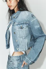 Cazadora de denim crop con cuello solapa, manga larga y cierre frontal con botones. Presenta efecto lavado, bolsillos de plastrón con solapa en el pecho y detalles de rotos.