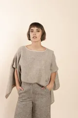 Poncho color beige con diseño a cuadros, cuello bote y terminaciones desflecadas. Tiene aberturas para los brazos en los laterales y detalles en cuero.