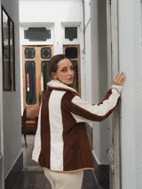 Campera con capucha, de tela tipo peluche a rayas verticales color marrón y blanco, con ribete color beige.