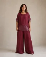 Blusa color bordó con cuello redondo y mangas cortas holgadas. Cuenta con detalles de lentejuelas brillantes en el dobladillo inferior y en los puños de las mangas.
