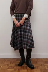 Falda midi de corte irregular con diseño a cuadros en tonos marrones, negros y beige. Presenta una silueta acampanada con caída fluida.