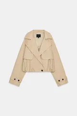 Trench corto de color beige con cuello de solapa y escote en pico. Presenta un diseño de cierre frontal cruzado con botones, mangas largas con trabillas en los puños y un bajo con acabado abullonado gracias a un elástico interior. Incluye bolsillos laterales ocultos y forro interior.