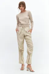 Pantalón de lino color beige, de corte relajado con elástico en la cintura y lazo ajustable. Presenta bolsillos laterales y detalle de presillas con botones en los tobillos para un ajuste regulable.