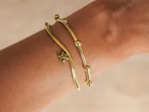 Pulsera rígida de bronce dorado con doble aro y detalle de zirconia verde.