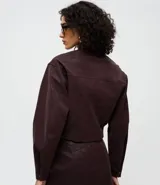 Campera de gamuza sintética color bordó, con diseño estructurado, cuello camisero, mangas largas y cierre frontal con botones cubiertos. Presenta dos bolsillos delanteros aplicados con solapa.