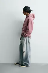 Sudadera tipo hoodie con cierre frontal de cremallera, diseño boxy fit, capucha ajustable con cordones, mangas largas con puños elásticos y bolsillos laterales. Presenta un acabado con efecto lavado.