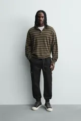 Pantalón cargo de corte slim fit en color negro, confeccionado en tejido de algodón con elasticidad. Presenta cintura elástica ajustable con cordón, bolsillos laterales tipo cargo con solapa y bajo acabado en puño elástico.