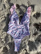 Traje de baño entero con estampado floral en tonos lila y rosa, con escote en V profundo y volados en los tirantes.