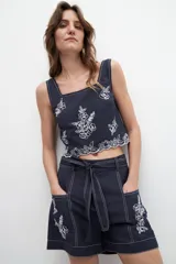 Top azul marino con breteles finos y escote cuadrado. Presenta bordados florales blancos en el frente y en el ruedo.