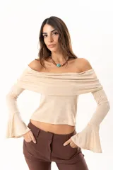 Blusa beige con hombros descubiertos, confeccionada en tela elástica con destellos de lurex. Presenta mangas largas con terminación acampanada y diseño ajustado al cuerpo.