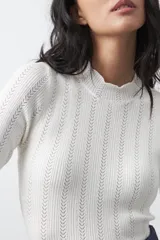 Polera de tejido de punto con textura calada y diseño de líneas verticales acanaladas. Presenta cuello alto y mangas largas con puños delicados, de silueta entallada.