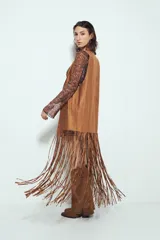 Chaleco largo de gamuza color marrón, con diseño abierto, flecos largos en el ruedo y apliques metálicos decorativos en el frente.