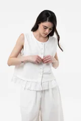Blusa sin mangas de color blanco, con botones frontales y detalle de volado en el ruedo, de corte relajado.