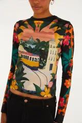 Remera de manga larga y cuello redondo de poliéster y elastano, con un llamativo estampado tropical que incluye un tranvía, vegetación y flores en tonos vibrantes sobre fondo negro.