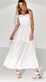 Vestido midi blanco de tela fluida con breteles finos decorados con borlas. Tiene corte imperio y falda con volantes.