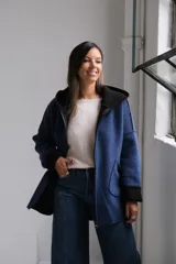 Tapado de paño azul con capucha, diseño de corte holgado y largo a la cadera. Presenta detalles en color negro en el interior, bordes y puños, con bolsillos frontales amplios y cierre frontal.