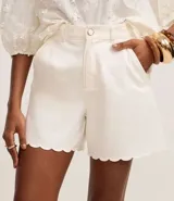 Short de sarga de algodón color blanco, con cintura alta, trabillas para cinturón, bolsillos delanteros y ruedo con acabado ondulado tipo nube. Marca Marfinno.