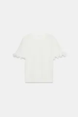 Camiseta blanca de algodón con cuello redondo, manga corta y detalle de aplicación de volantes en las mangas.