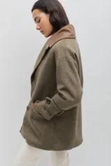 Tapado de paño de lana color marrón con silueta oversize y hombros caídos. Presenta doble abotonadura frontal, solapas amplias con detalle en contraste azul, y mangas con ajuste en los puños.