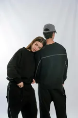 Buzo negro de corte holgado con cuello redondo, confeccionado en frisa invisible premium. Presenta detalles de vivos en color blanco en los laterales y en la espalda, y cuenta con una etiqueta decorativa en el frente.