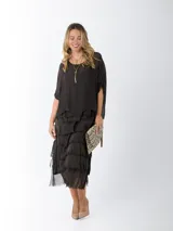 Vestido midi de seda italiana color negro, diseño dos en uno con capa superior de calce amplio, falda con volados y forro interior de algodón elastizado.