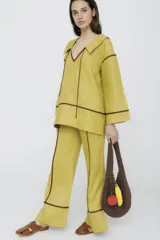 Pantalón de vestir color manteca, de corte recto y tiro alto, con detalle de ribetes marrones en los laterales.