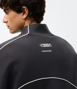 Buzo deportivo de corte boxy, color negro, con cuello alto, cierre frontal completo y mangas largas. Presenta detalles de líneas blancas a lo largo de las mangas y lettering estampado en el pecho.