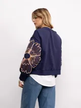 Buzo de algodón color negro con cuello redondo, mangas largas y bordado floral XL en color cobre en las mangas. Presenta un diseño holgado y cómodo.