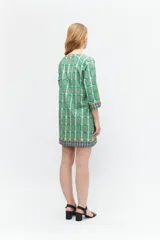 Túnica verde con estampa geométrica de cuadrados en verde más oscuro y blanco. Tiene escote en V con ribete marrón y mangas tres cuartos con ribete geométrico en puños y ruedo.