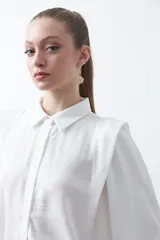 Camisa negra de estilo sastrero con cuello clásico, frente abotonado y mangas largas con puños ajustados. Presenta un diseño con hombreras sutiles que aportan estructura a la prenda.