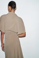 Top fluido color beige, con cuello perkins y mangas por debajo del codo. Bajo redondeado.